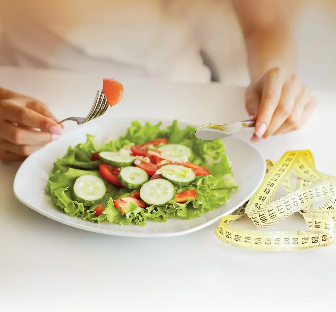 Person eating a fresh salad beside a tape measure, representing medically guided weight management