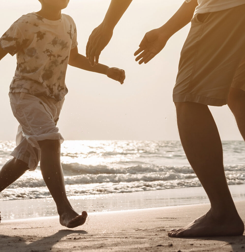Parent and child walking along Bang Saen beach at sunset